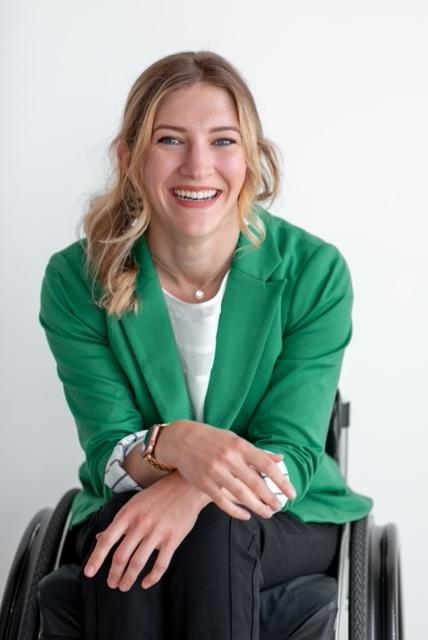 丽兹·拉根穿着绿色运动上衣和黑色裤子坐在轮椅上
